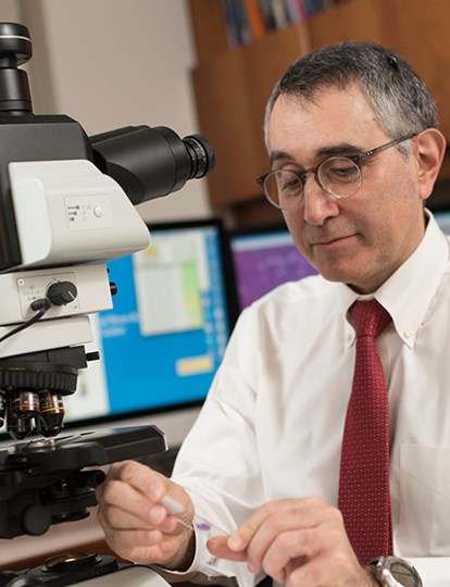 MSK Colleague in shirt and tie sat by a microscope and looking at a microscope slide